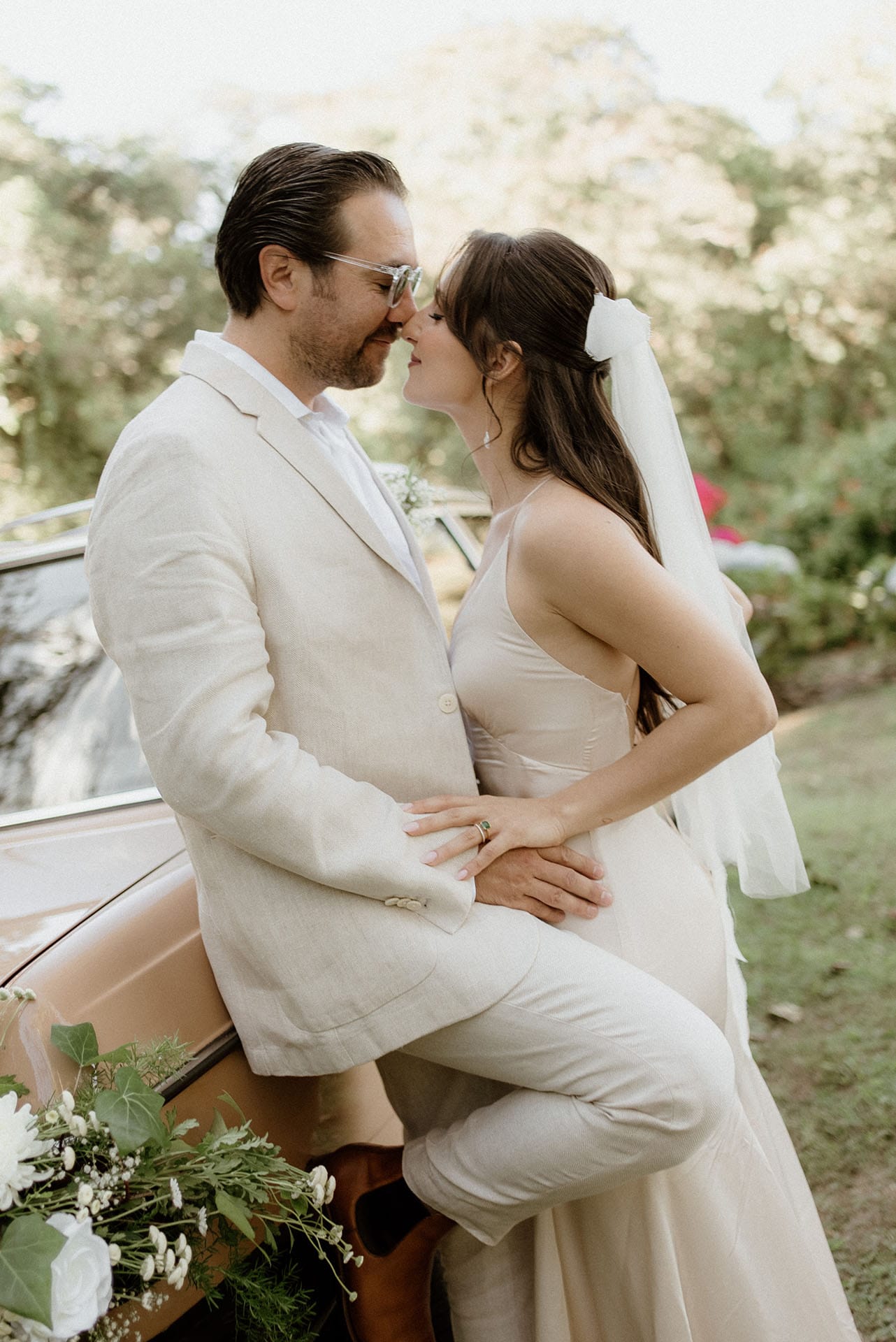 Bride and groom embrace by vintage car