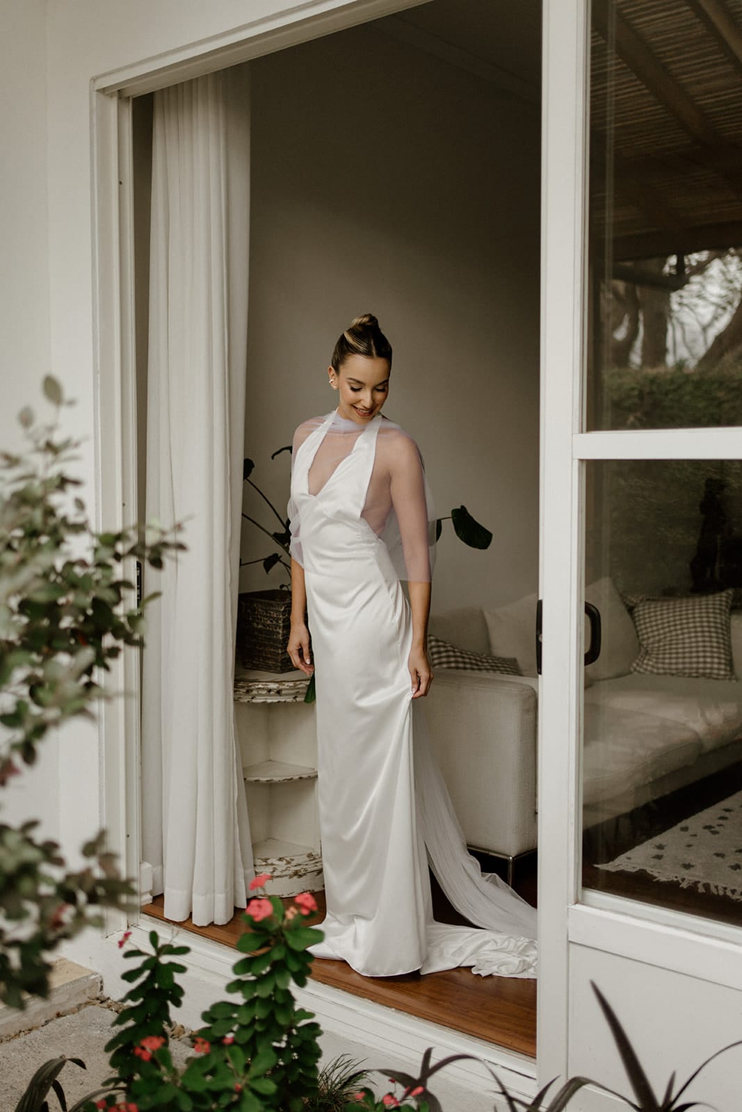 Bride in gown with veil stands in window doorway