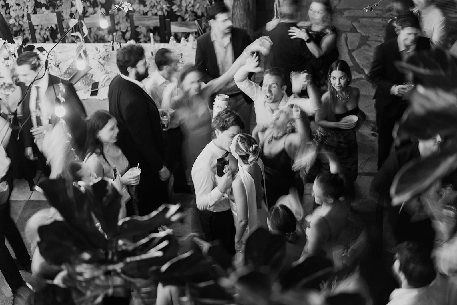 Bride and groom kiss in the middle of a crowd during reception